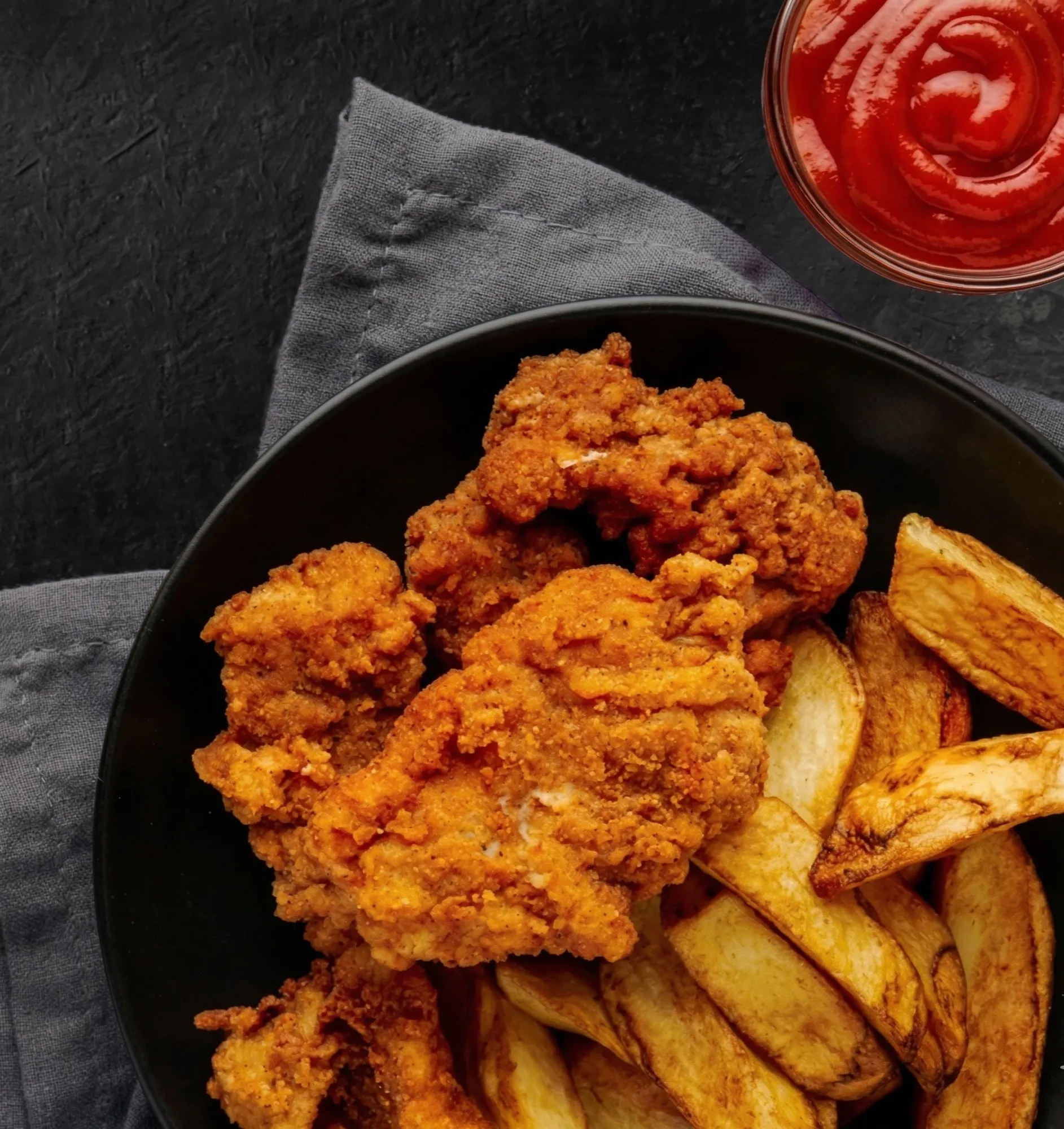 A bowl of Round Haus Famous Fried Chicken with seasoned potato wedges and dipping sauce.