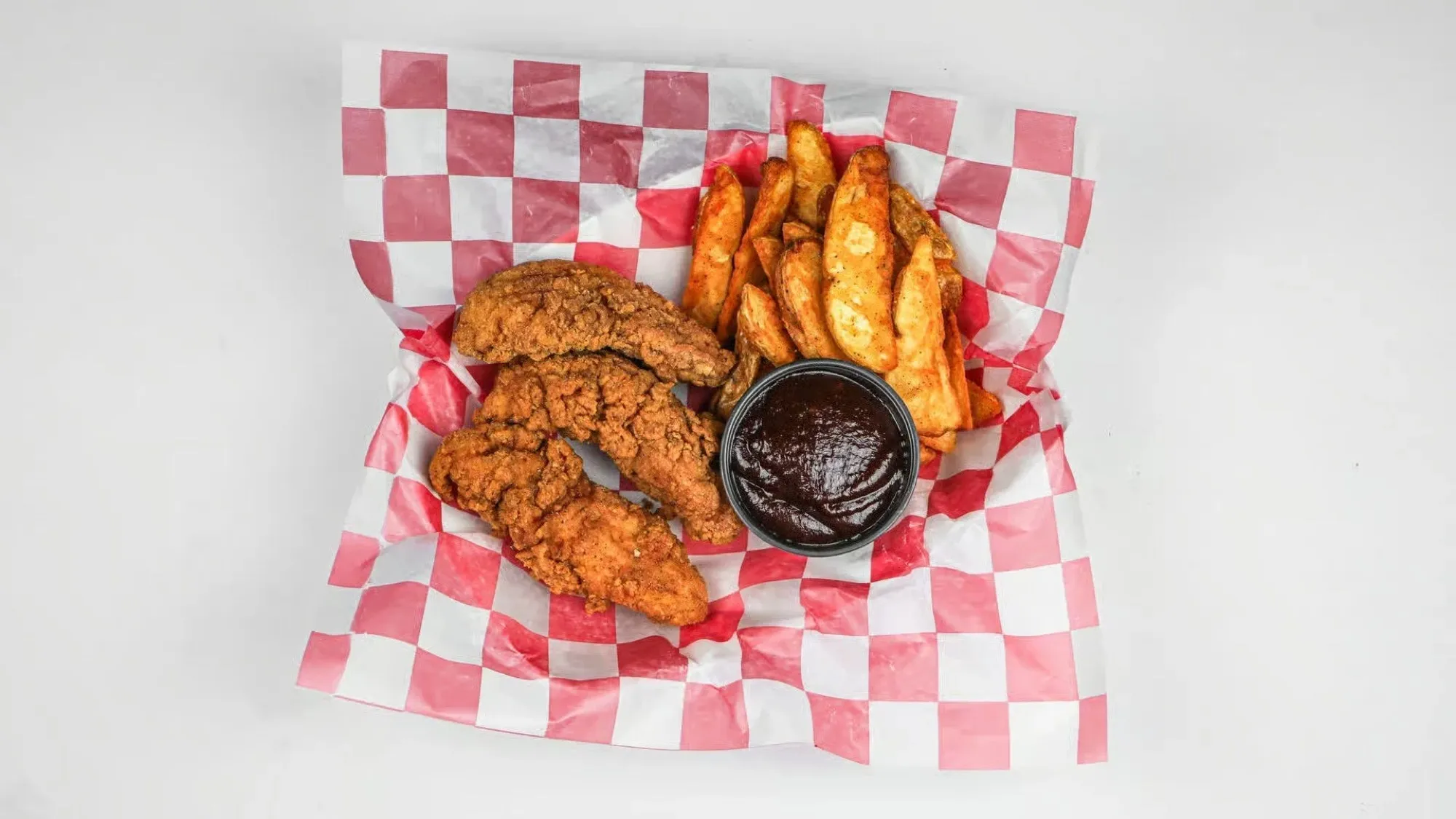 Round Haus chicken tenders and potato wedges served in a checkered paper basket.